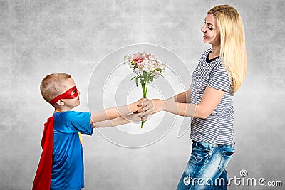 The son in the costume of a superhero gives his mother a bouquet of flowers. Stock Photo