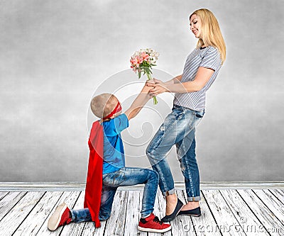 The son in the costume of a superhero gives his mother a bouquet of flowers. Stock Photo