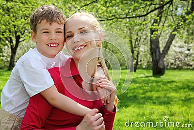 Son embraces behind mother in park Stock Photo