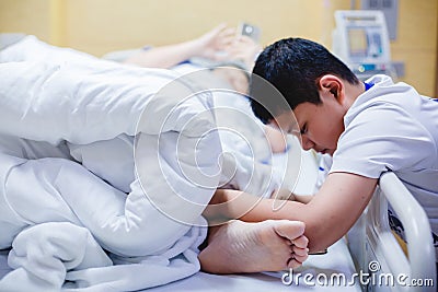 The son is taking care of the sick mother on the hospital bed. The boy is massaging his mother`s legs. female patients lying in Stock Photo
