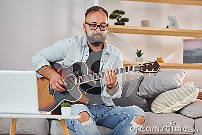 Songwriting process. Man in casual clothes and with acoustic guitar is indoors Stock Photo