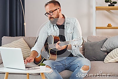 Songwriting process. Man in casual clothes and with acoustic guitar is indoors Stock Photo