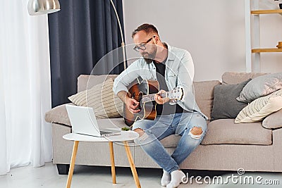 Songwriting process. Man in casual clothes and with acoustic guitar is indoors Stock Photo