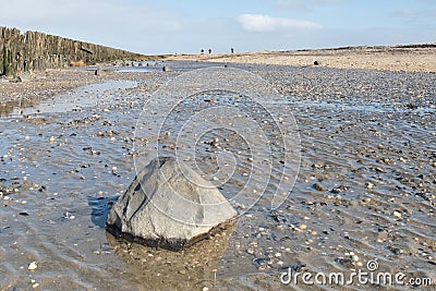 A soothing picture of the wadden sea at paesens moddergat, big rock in foreground, sea and sky, people in the distance Stock Photo