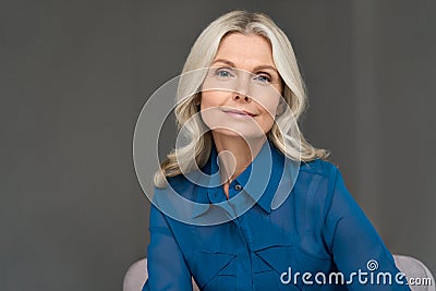 Sophisticated 50s middle aged woman model sitting in chair looking at camera. Stock Photo