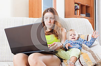 Sorehead mother with crying toddler working online Stock Photo