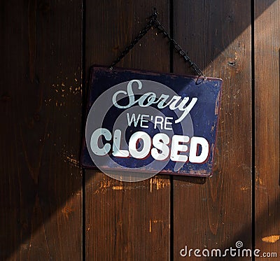 Sorry we`re closed, blue and white sign on old wooden door, with a shadow that divides it into a clear and dark part Stock Photo