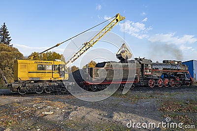 Railway crane KZh-462 `Pervomaets` loads with coal the old soviet steam locomotive Editorial Stock Photo