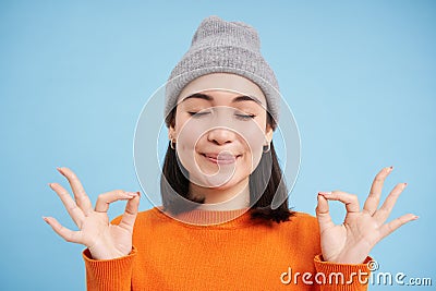 Sounds mind in healthy body. Smiling calm and relaxed asian girl in beanie, shows zen, relaxation gesture, meditating Stock Photo