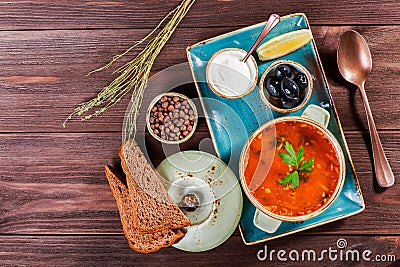 Soup with meat, olives, herbs, lemon, sour cream in bowl, black bread and spices on dark wooden background, homemade food Stock Photo