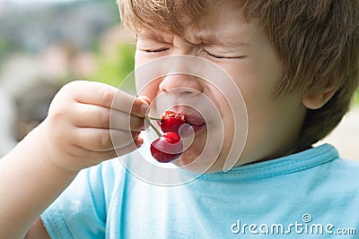Sour. Sour taste. A child tastes a cherry. Ripe harvest. Vitamins. Sour cherry. Stock Photo