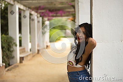 South American woman, young, beautiful, brunette, with crochet top and jeans leaning on a column, with a tender and dreamy look. Stock Photo