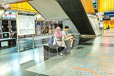 One Muslim female wearing hijab, one Asian male teen sitting on bench in subway station Editorial Stock Photo