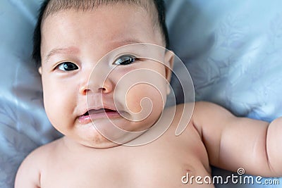 South East Asian new born isnâ€™t wearing shirt. Newborn face is upset. Baby is laying on the bed. Infant is 4 months old. Stock Photo