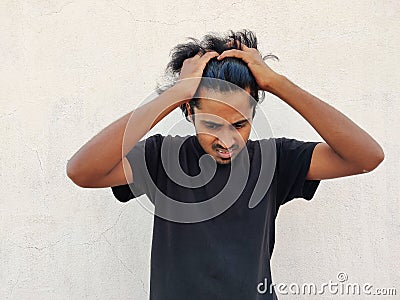black tshirt rending his hair, looking down and feeling sad ,holding hands on head. White Stock Photo