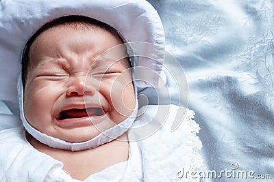 Southeast Asian baby colic is wearing white hat and shirt. South East Asian newborn is crying. Newborn is unhealthy. Stock Photo