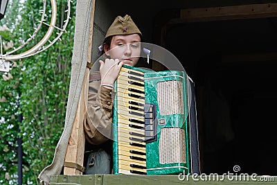 Soviet female soldier in uniform of World War II with an accordion sitting in a military truck on Victory Day in Volgograd Editorial Stock Photo