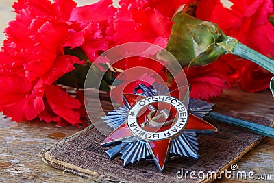 Soviet order of Patriotic War inscription Patriotic war with red carnations on an old wooden table. May 9 day of victory in the Stock Photo