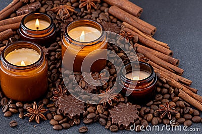 Soy scented candle in a jar. Coffee beans, anise, cinnamon spices. The candles are burning. Dark background. Stock Photo