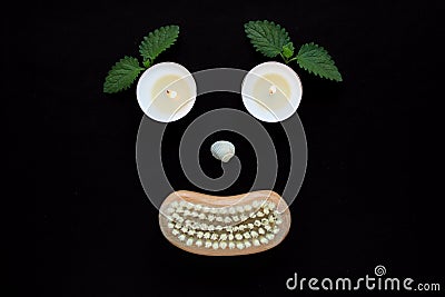 Spa wellness concept, face with eyes candles, a seashell nose and a mouth of a wooden body brush on black background Stock Photo