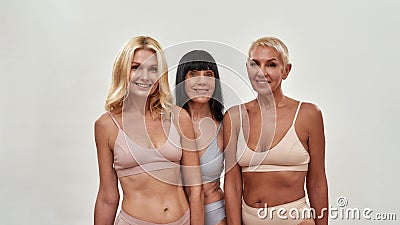 Spa day. Three happy mature women in underwear smiling at camera while posing half naked in studio against light Stock Photo