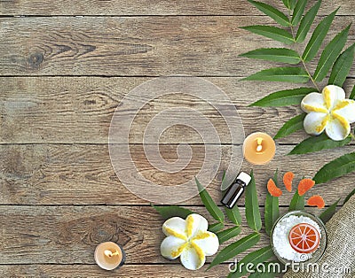 Spa products border. Sea salt in bowl, palm leaves, aroma oil, plumeria and citrus homemade soap, candles on wooden background. Stock Photo