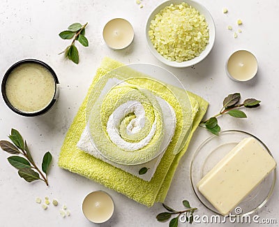 Spa products composition with sea salt, scrub, soap and bath towels on a white stone background with candles and green leaves. Stock Photo