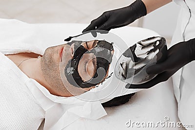 Spa therapy for men receiving facial black mask. Stock Photo