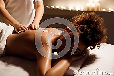 Spa treatment. Beauty therapist pouring salt scrub on womans back Stock Photo