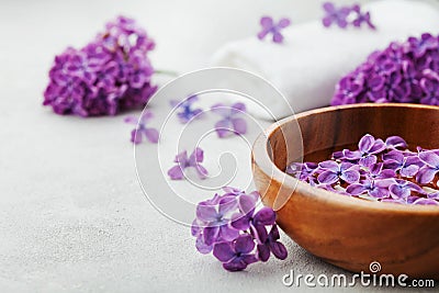 Spa and wellness composition with perfumed lilac flowers water in wooden bowl and terry towel on stone background, aromatherapy Stock Photo
