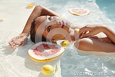 SPA Woman In Pool With Citrus. Beautiful Girl With Fresh Tropical Fruit Relaxing At Resort. Stock Photo