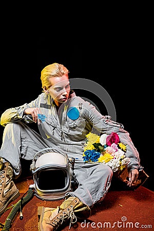 spacewoman in spacesuit with helmet and flowers in paper bag sitting on red Stock Photo