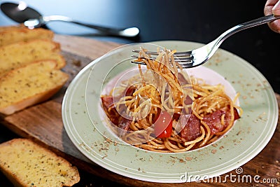 Spaghetti bacon with fork in hand and tomato in the green and white color plate and Garlic bread on wooden table background. Foods Stock Photo