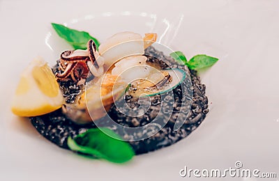 Spaghetti black rice with seafood in sause with lemon slice. spaghetti with scallops shells squid ink with prawns, mussels and par Stock Photo