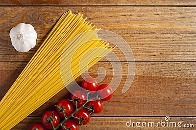 Spaghetti, cherry tomatoes and head of garlic on a brown wooden table. Tomatoes to the right of spaghetti, garlic to the left. Top Stock Photo