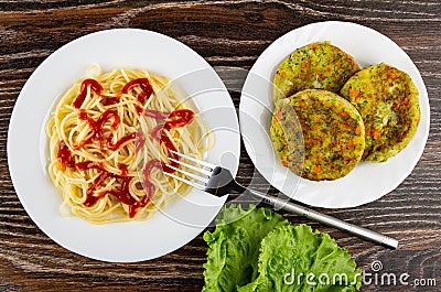 Spaghetti with ketchup in plate, fork, vegetable cutlets in plate, leaves of lettuce on wooden table. Top view Stock Photo