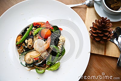 Spaghetti with prawns and seafood on white plate, black spaghetti with seafood on table in restaurant, spicy spaghetti in food Stock Photo