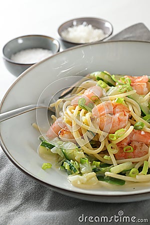 Spaghetti , shrimps, zucchini and spring onions, a healthy Mediterranean meal in a grey plate with a fork, napkin and spice bowls Stock Photo