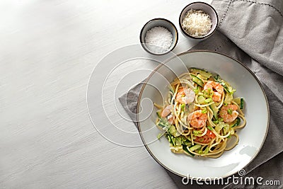 Spaghetti with zucchini courgettes, spring onions and prawns in a grey plate on a white painted table, napkin and small salt and Stock Photo