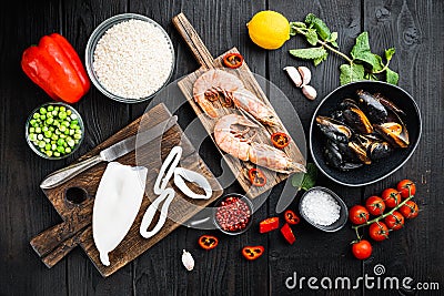 Spanish seafood paella ingredients, rice,prawns, mussels, peas on black wooden background, flat lay Stock Photo