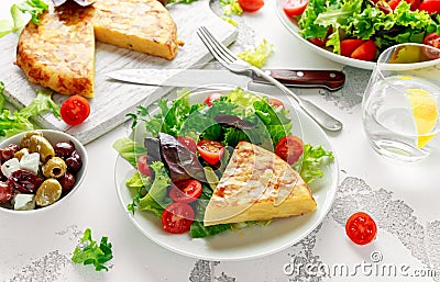 Spanish tortilla, omelette with potato, onion, vegetables, tomatoes, olives and herbs in a white plate. breakfast Stock Photo