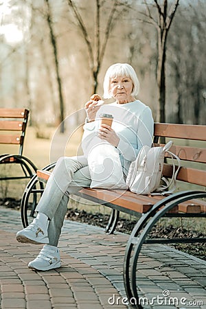 Fascinating beaming senior female eating cookies and drinking coffee Stock Photo