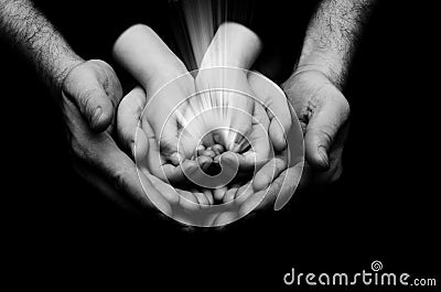 Spark of hope in a child hands wh holding by parents handson dark background. The light of faith Stock Photo