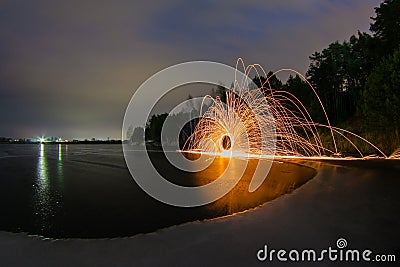 Sparks from the burning steel wool against the backdrop of a frozen lake Stock Photo