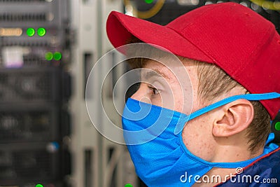 The specialist is in the datacenter during the quarantine. Portrait of a masked teenager in close-up. A technician in a red cap Stock Photo