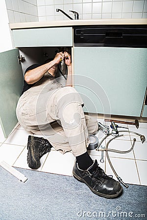 Specialist male plumber repairs faucet in kitchen Stock Photo