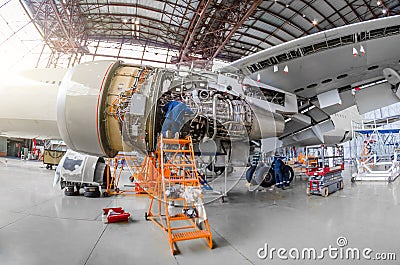 Specialist mechanic repairs the maintenance of a large engine of a passenger aircraft in a hangar. View of engine without bonnet, Stock Photo