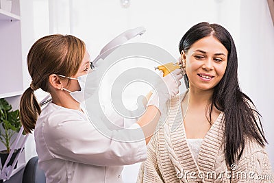 Specialist in medical mask and gloves pierces the client& x27;s ears with a piercing gun in the cosmetologist cabinet. Stock Photo