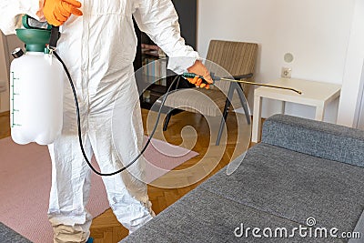 Person in protective suit with decontamination sprayer bottle disinfecting household and furniture Stock Photo