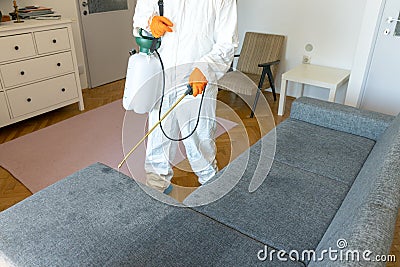 Person in protective suit with decontamination sprayer bottle disinfecting household and furniture Stock Photo